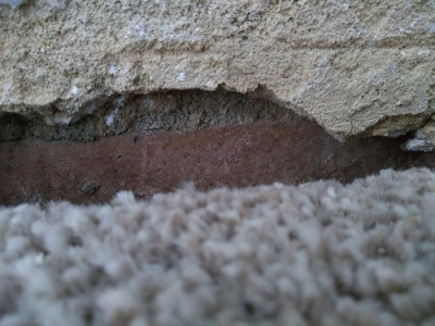 Plaster gap in wall extends below the carpet level.